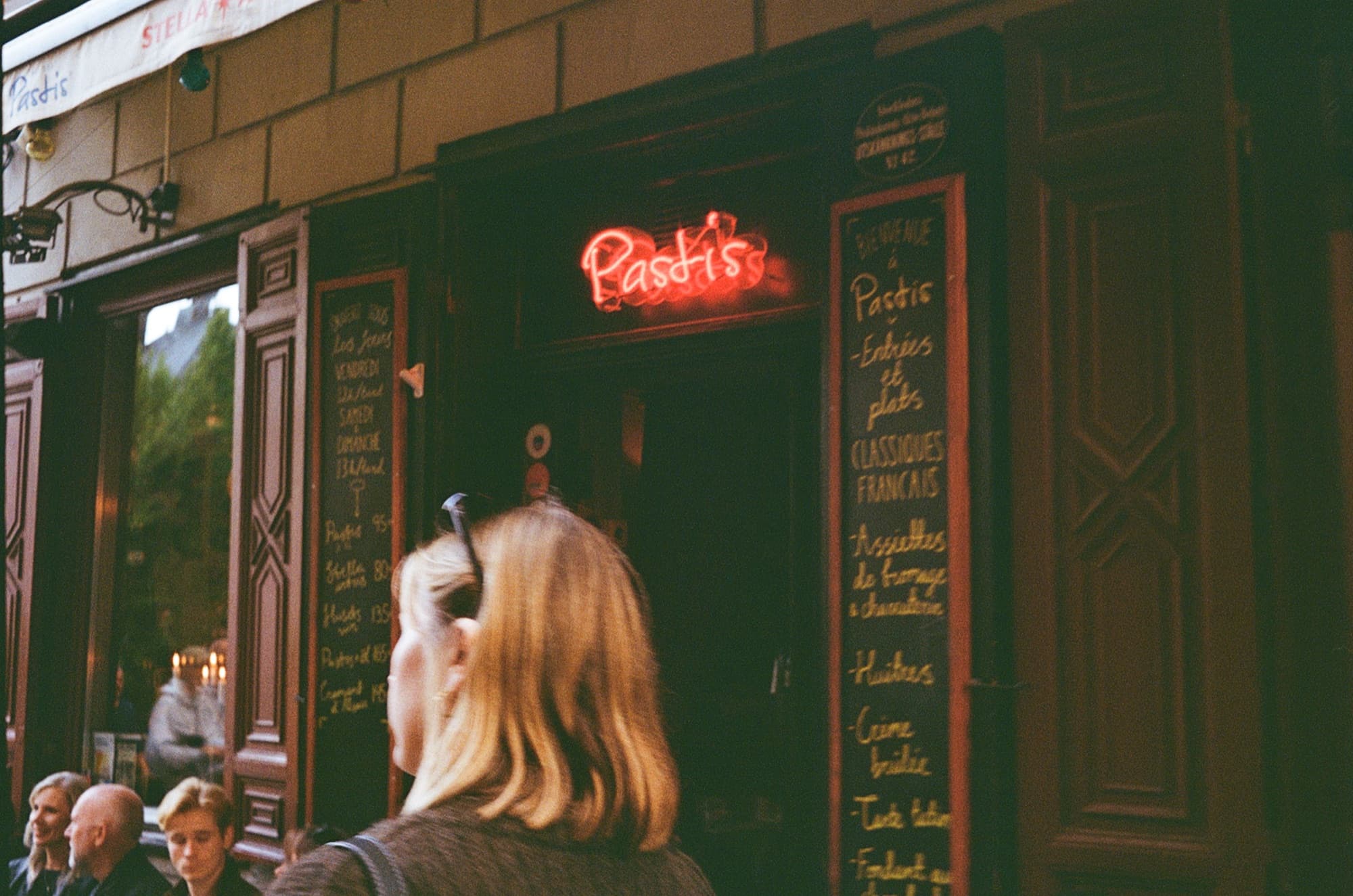 Someone looking up at a neon sign and chalkboard menus outside a small café