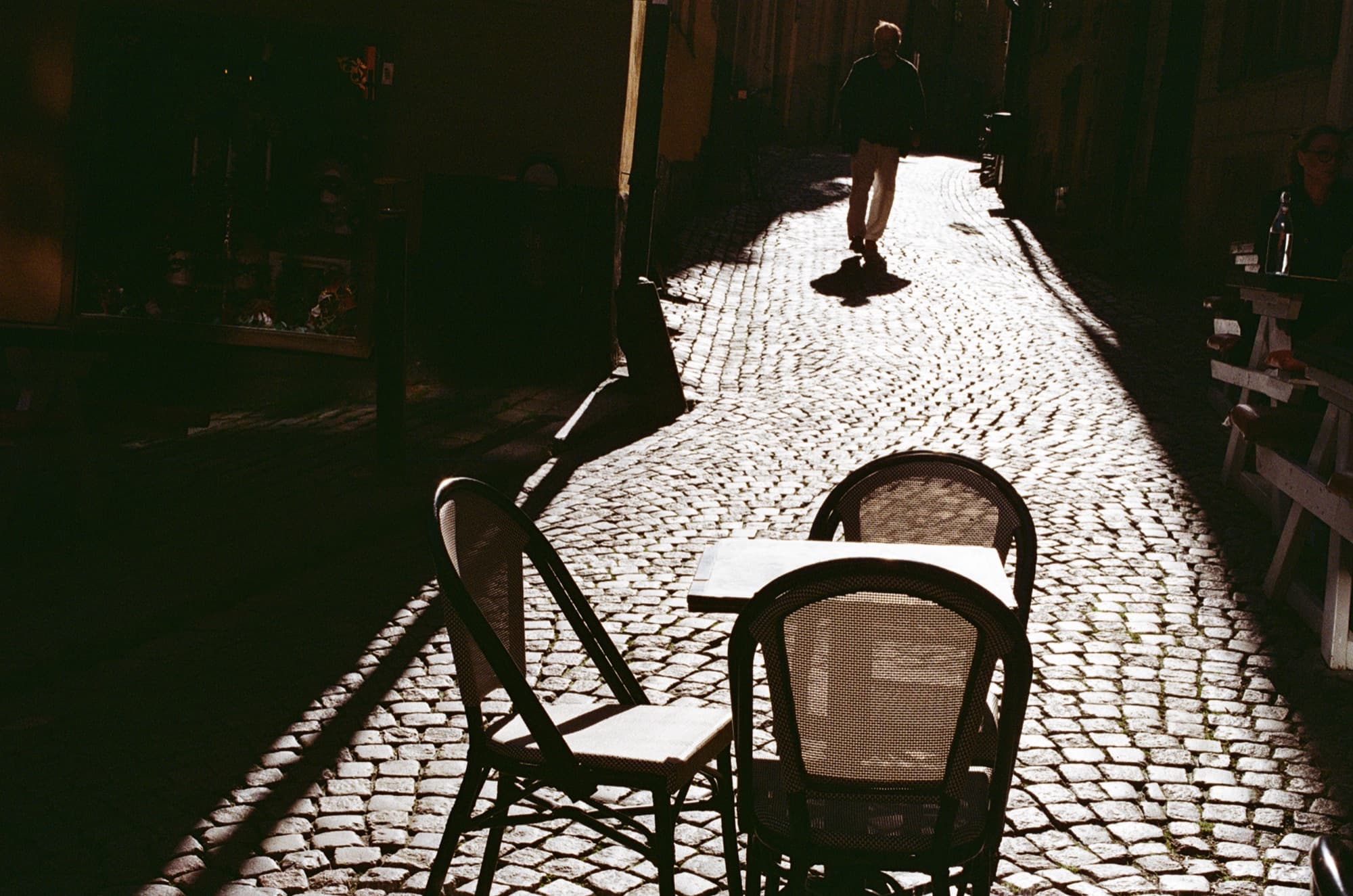 An empty café table and chairs on a sunlit cobbled lane